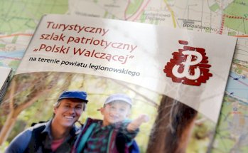 Fragment okładki przewodnika Szlaku Polski Walczącej, na zdjęciu dososły mężczyzna z dzieckiem w stroju do wędrowania, w tle las, napisy Turystyczny Szlak Patriotyczny Polski Walczącej, logo Szlaku PW